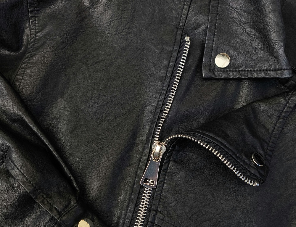 Close-up of a black leather jacket, showing a silver zipper partially unzipped and metallic snap buttons on the collar and lapel.
