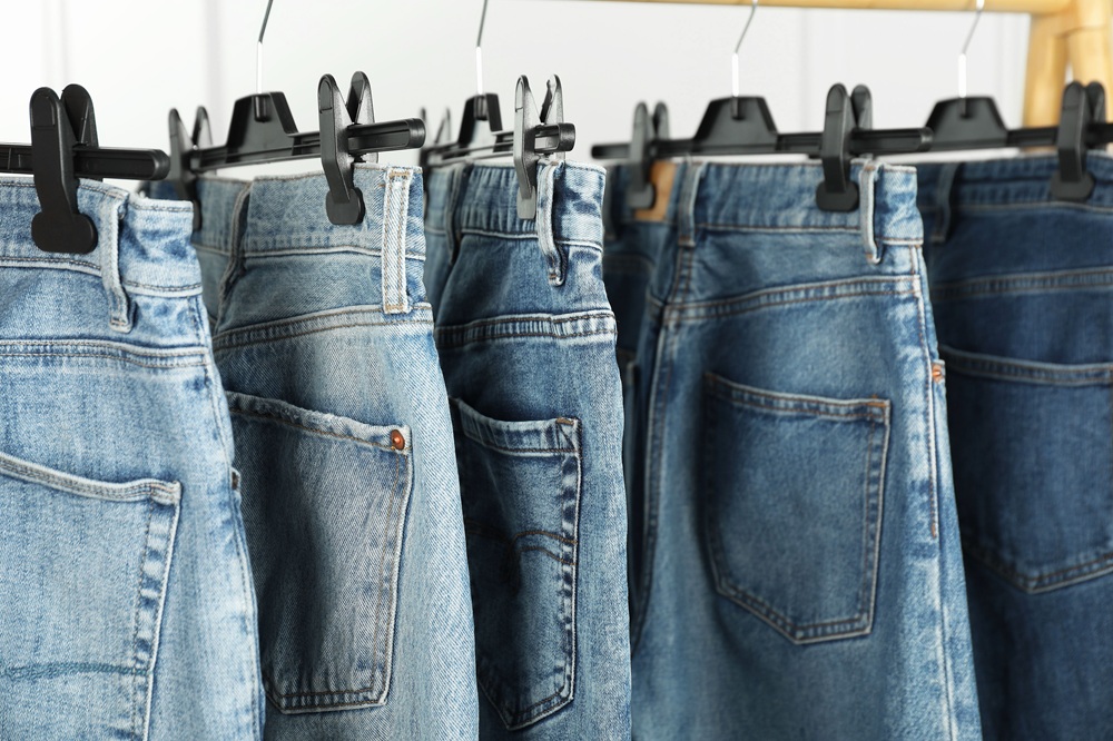 Several pairs of blue jeans are hanging on black plastic hangers, displayed in a row on a clothing rack.