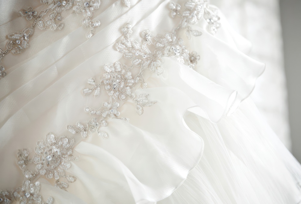 Close-up of a white wedding dress with ruffled layers and intricate bead and sequin floral embroidery.